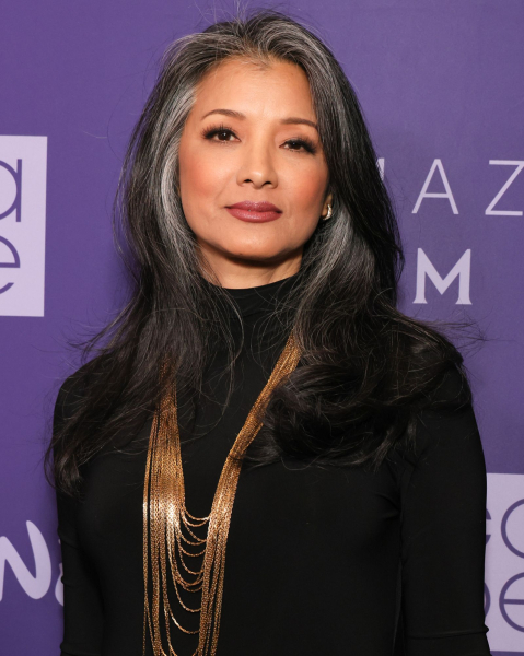 Kelly Hu posing in a black turtleneck and layered gold necklaces